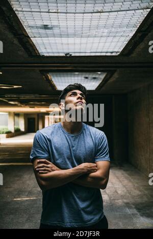 Thoughtful young man with arms crossed standing in basement Stock Photo