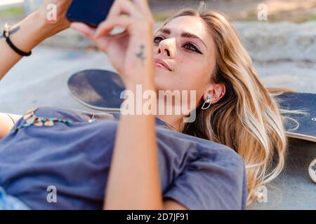 Beautiful woman using smart phone while lying on skateboard over road Stock Photo