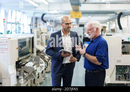 Businessman holding digital tablet while looking at senior manager discussing at illuminated factory Stock Photo