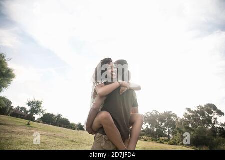 Young woman embracing man carrying her in arms while standing at public park Stock Photo