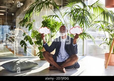 Mature man laughing while holding speech bubble with cross legged sitting at home Stock Photo