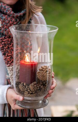 Close-up of young woman holding container with candle and pine cones while standing outdoors Stock Photo