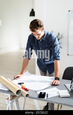Architect analyzing blueprint while standing by desk at office Stock Photo