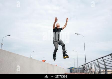 Young man with inline skates jumping on bridge against sky Stock Photo