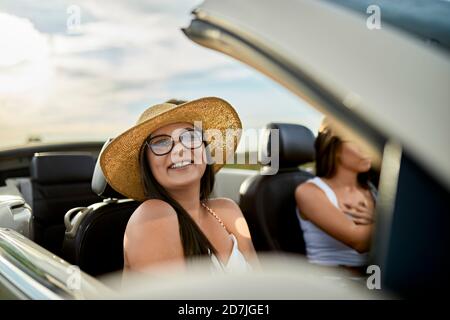 Young smiling woman traveling with friend in convertible car