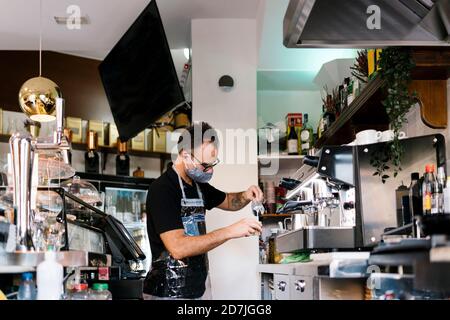 Male barista wearing protective face mask while working in cafe during COVID-19 crisis Stock Photo