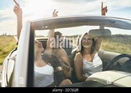Young female friends having fun while dancing in convertible car Stock Photo