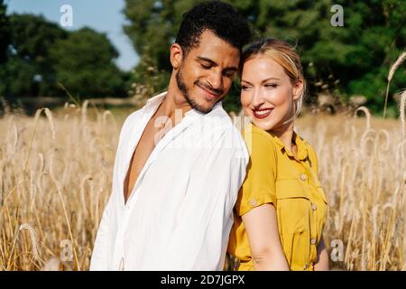 Smiling man and woman looking at each other while standing back to back on meadow Stock Photo