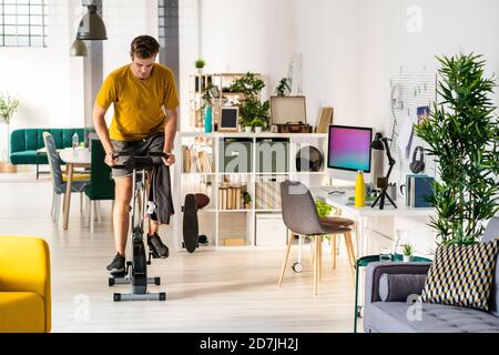 Young man looking down while cycling on exercise equipment at home Stock Photo