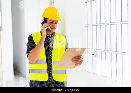 Smiling architect holding notepad while talking on mobile phone at office under construction Stock Photo