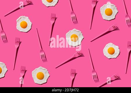 Pattern of pink plastic forks and fried eggs against pink background Stock Photo