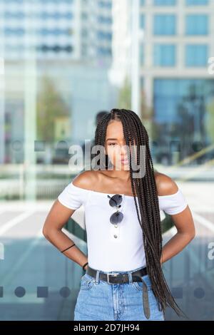 Young woman with hand behinds back standing against glass wall in city Stock Photo