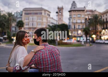 Couple wearing protective mask sitting on street in city Stock Photo