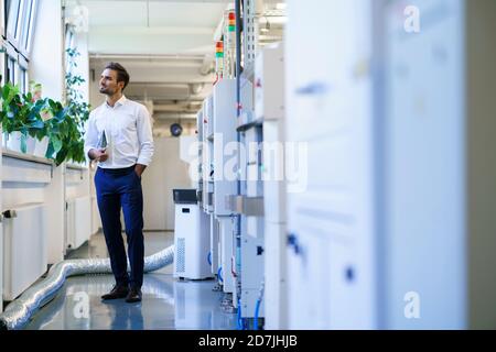 Thoughtful male technician holding digital tablet while looking away at illuminated factory Stock Photo