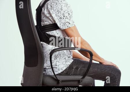 closeup of a young caucasian man wearing an upper back posture corrector as is sitting at his office chair Stock Photo