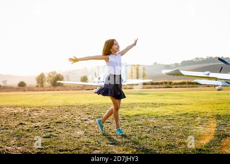 Little girl with arms outstretched standing at airfield Stock Photo