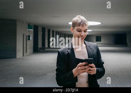 Smiling trans young man using mobile phone while standing in basement Stock Photo