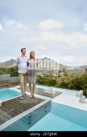 Heterosexual couple looking away while standing in balcony of modern house Stock Photo