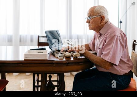 Retired senior man using magnifying glass for research of fossil and mineral at home Stock Photo