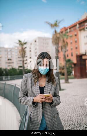 Young woman text messaging on smart phone while standing in city Stock Photo