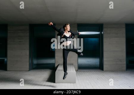 Non-binary young man wearing black suit dancing in basement Stock Photo