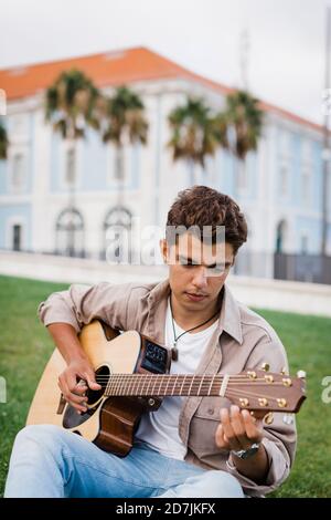 Handsome young man practicing guitar while sitting on grass at park Stock Photo