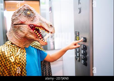 Close-up of boy wearing dinosaur mask and cape pushing buttons in elevator Stock Photo