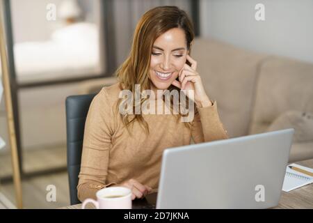 Businesswoman smiling while working on laptop at home Stock Photo