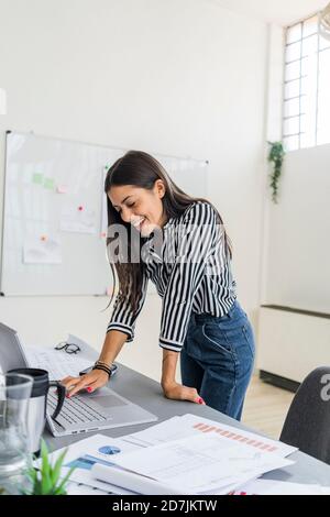 Smiling young female design professional using laptop at desk while working in creative office Stock Photo