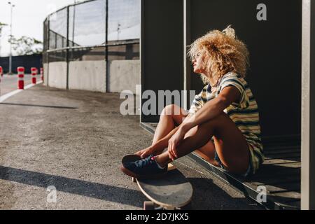 Thoughtful woman sitting with skateboard while looking away on sunny day Stock Photo