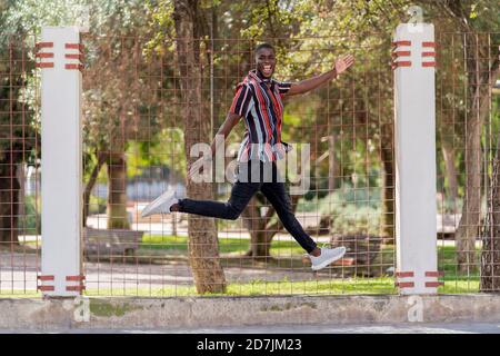 Cheerful young man jumping against fence at park Stock Photo