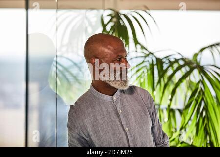Thoughtful bald male freelancer looking away while leaning on glass wall at rooftop Stock Photo