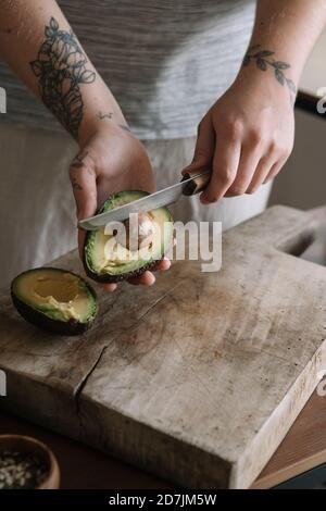 Woman cutting avocado while standing in kitchen at home Stock Photo