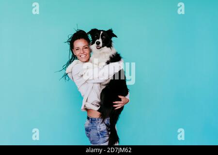 Happy woman carrying Border Collie dog against turquoise background Stock Photo