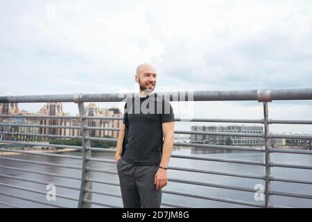 Smiling young man looking away while standing against railing on bridge in city Stock Photo