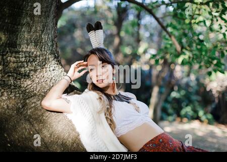 Fashionable woman with feather in hair leaning on tree Stock Photo
