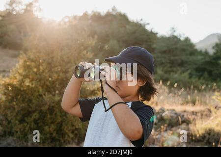 Boy looking at view through binocular while standing at mountain Stock Photo