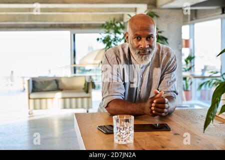Confident bald man with hands clasped leaning on table at rooftop Stock Photo