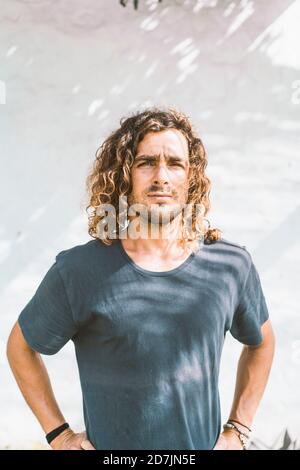 Serious young man with hands on hip standing against white wall Stock Photo