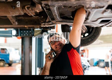 Mechanic talking over mobile phone while repairing car in workshop Stock Photo