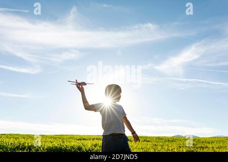 Playful boy holding airplane toy while standing against clear sky Stock Photo