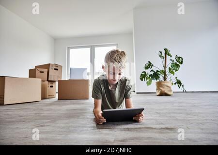 Boy lying down while playing on digital tablet in new house Stock Photo