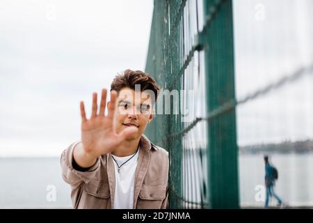 Handsome young man showing hand by metallic fence Stock Photo