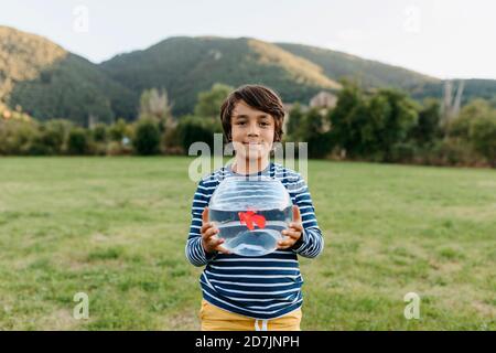 Smiling boy holding fishbowl in hand while standing at back yard Stock Photo