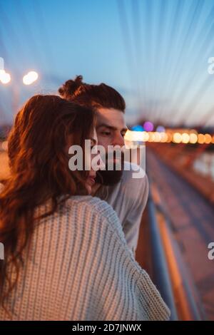Thoughtful couple looking away while standing on bridge in city at dusk Stock Photo