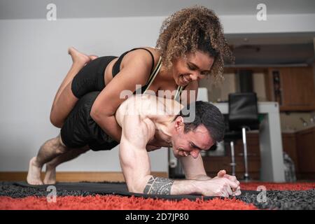 Smiling woman lying on man's back while exercising at home Stock Photo