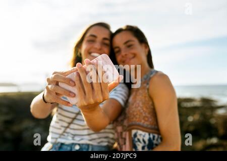 Happy young sisters taking selfie through smart phone at beach during weekend Stock Photo