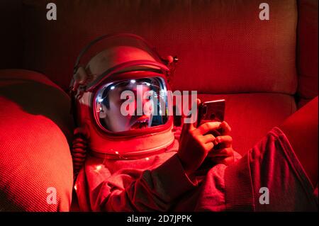 Close-up of boy wearing space helmet using mobile phone while relaxing on sofa in illuminated home Stock Photo