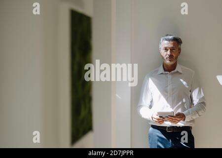 Man using digital tablet while leaning on wall at office Stock Photo