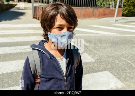 Schoolboy wearing mask standing on road during sunny day Stock Photo